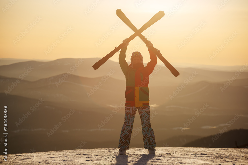 Fototapeta premium A skier holds skis in his hands against the sunset sky.