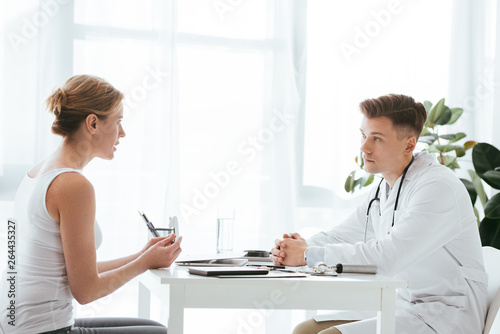 handsome doctor in white coat looking at attractive patient in clinic