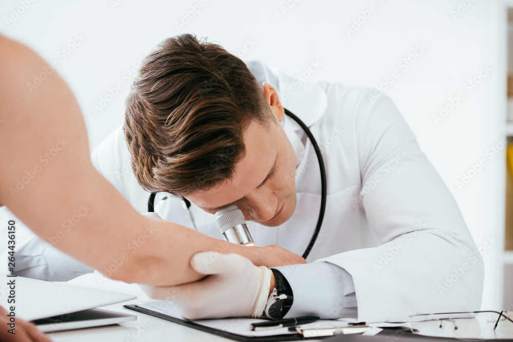 selective focus of dermatologist examining hand of woman while holding dermatoscope selective focus of dermatologist examining hand of woman while holding dermatoscope