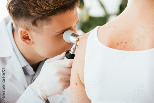 dermatologist in latex gloves holding dermatoscope while examining patient with skin disease