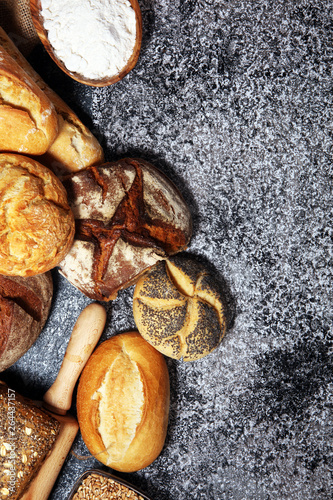 Assortment of baked bread and bread rolls on rustic grey bakery table background © beats_