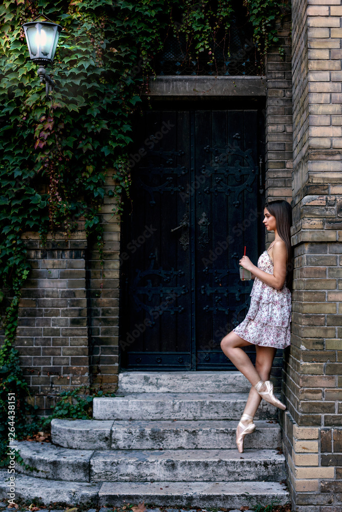 Young beautiful long hair ballet dancer standing at stairs and drink juice from jar Young beautiful long hair ballet dancer standing at stairs and drink juice from jar
