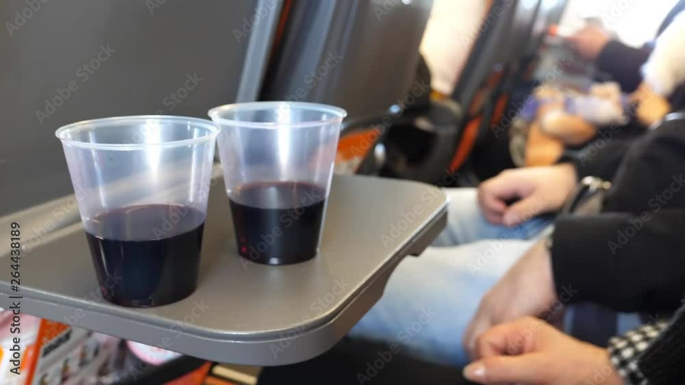Close up of two plastic glasses with red wine on airplane tray table in-flight, blurry people, passengers in the background