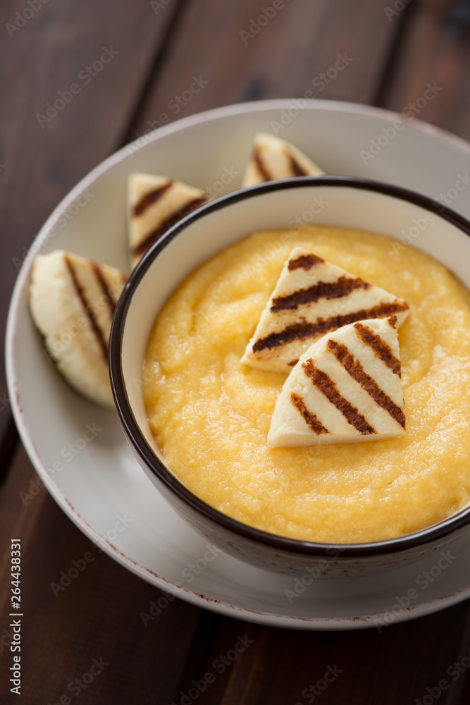 Bowl of polenta served with grilled cheese, vertical shot on a rustic wooden background, closeup