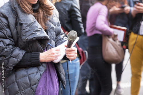 Female journalist at news conference  writing notes  holding microphone