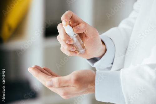 cropped view of doctor applying antibacterial spray on hand in hospital
