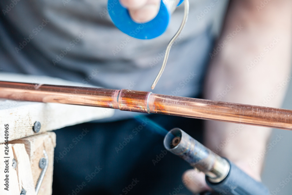 Closeup professional master plumber holding flux paste for soldering and brazing seams of copper pipe gas burner. Concept installation and repair of an apartment building pipeline, leakage Closeup professional master plumber holding flux paste for soldering and brazing seams of copper pipe gas burner. Concept installation and repair of an apartment building pipeline, leakage
