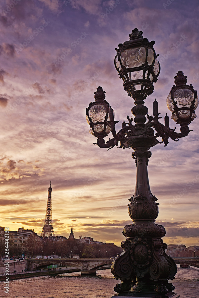 Eiffel Tower in background at sunset with lamp post from bridge in Paris, France.