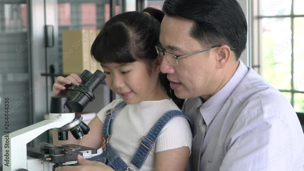 Teacher and little girl is looking through microscope in modern laboratory of school. Concept of science, testing development and lab industry.