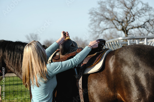 Girl with horse putting on saddle to go horseback riding.