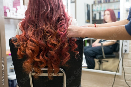 Hairdresser's hands make the formation of curls of long hair on the head of the client in the salon.