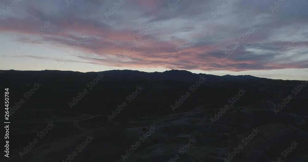 Drone shot pulling back out away from silhouetted mountains and sunset over brush and winding desert roads. Drone shot pulling back out away from silhouetted mountains and sunset over brush and winding desert roads.