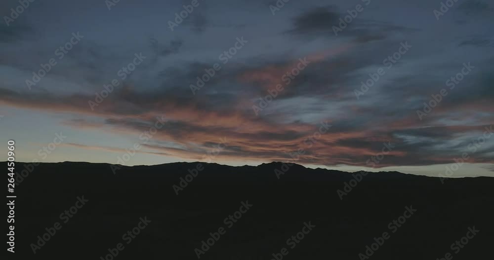 Static drone shot looking at silhouetted mountains and colorful sunset in desert during spring.