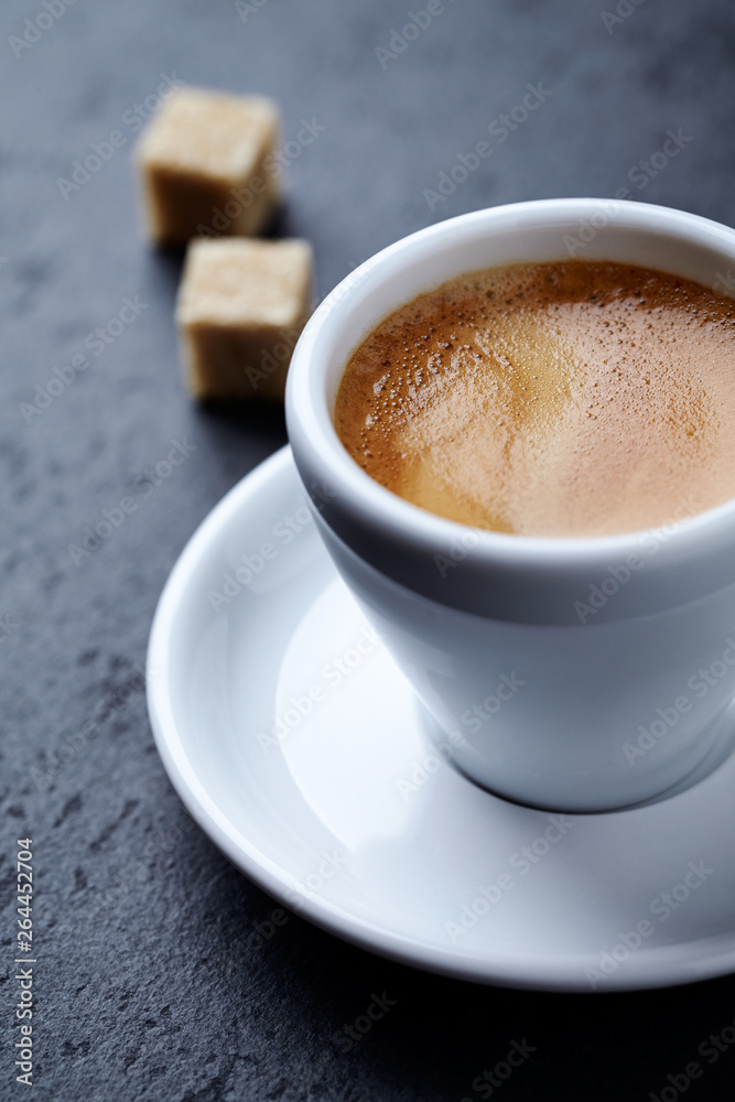 Cup of coffee and two brown sugar cubes on dark stone background. Close up. Cup of coffee and two brown sugar cubes on dark stone background. Close up.