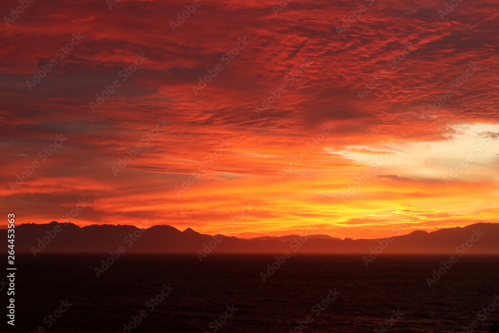 Beautiful bright orange sunrise over a bay with mountains in the background.