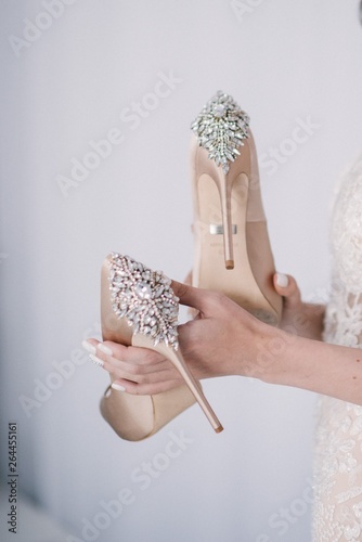 Bride in a white wedding dress holding wedding shoes in her hands