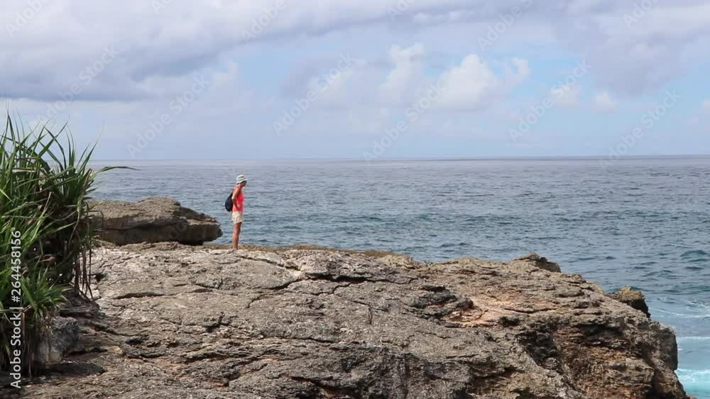 A women admiring the turquoise water and waves at the cliffs edge on Ceningan island in Indonesia. A women admiring the turquoise water and waves at the cliffs edge on Ceningan island in Indonesia.