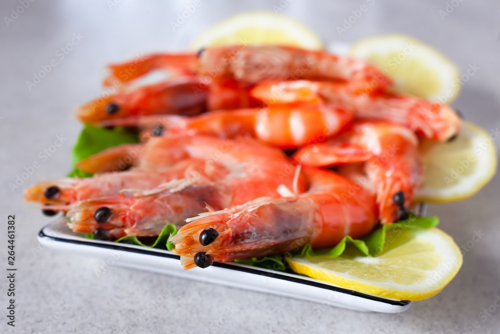 a plate of boiled shrimps with lemon close up, on a light gray table