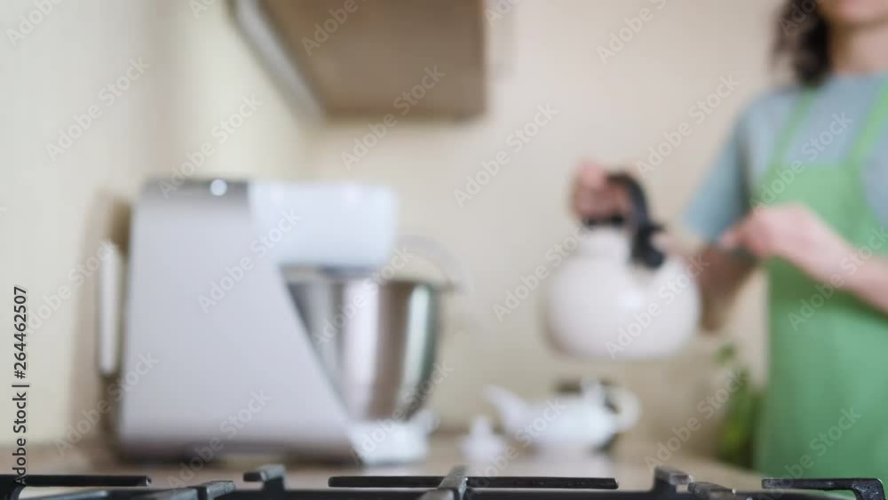 A woman in the kitchen brewing tea. A woman pours hot water into a kettle. Tea preparation. A woman in the kitchen brewing tea. A woman pours hot water into a kettle. Tea preparation.
