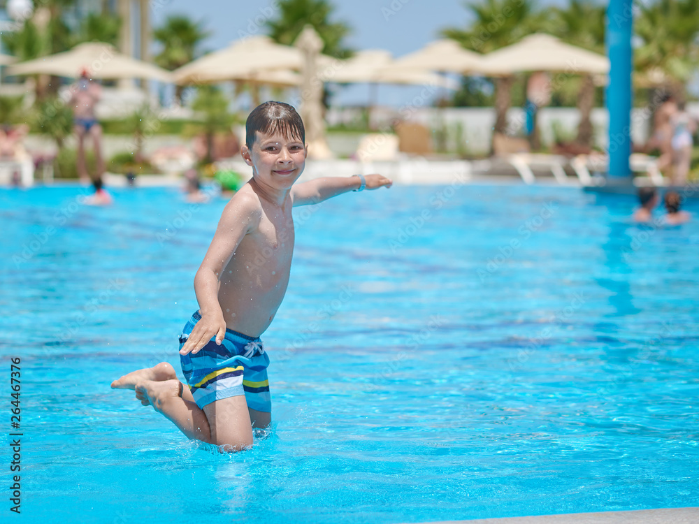 European boy jumping into swimming pool at resort. Moment of entrance in water.