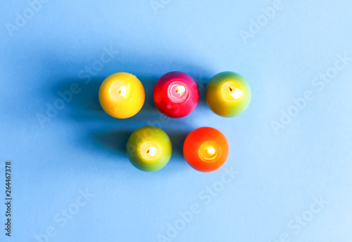 Bright burning paraffin candles in the shape of colorful Easter eggs on blue background.