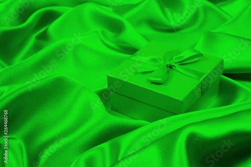 Green gift box on green silk. Greeting card bakcground.