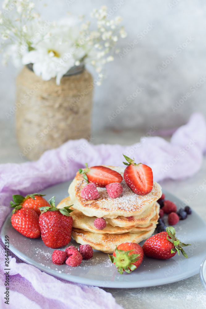 Fritters with strawberries, blueberries and raspberries on a gray plate front view against the background of a concrete wall and white flowers Fritters with strawberries, blueberries and raspberries on a gray plate front view against the background of a concrete wall and white flowers