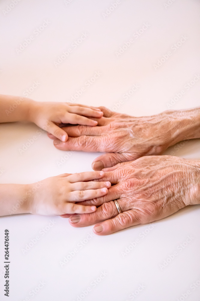 An elderly woman (old lady, grandmother) holds her little granddaughter's small hands. Family unity, love, help, assistance. Age and generational difference. Aged and wrinkled hands with young hands. An elderly woman (old lady, grandmother) holds her little granddaughter's small hands. Family unity, love, help, assistance. Age and generational difference. Aged and wrinkled hands with young hands.