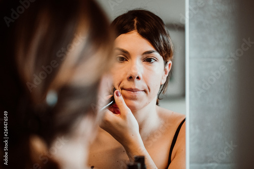 .Young and pretty short-haired woman putting on makeup in front of the mirror in her house in the morning. Lifestyle.