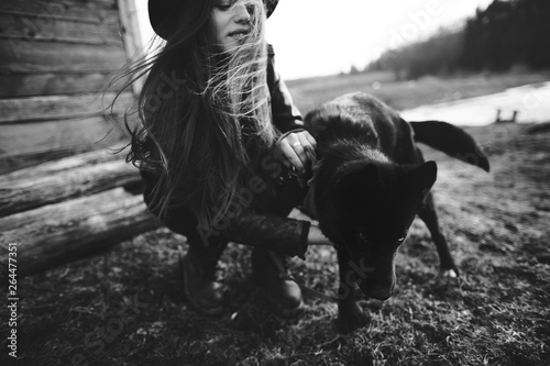 Happy young woman plaing with her black dog in fron of old wooden house. Black and white photo photo