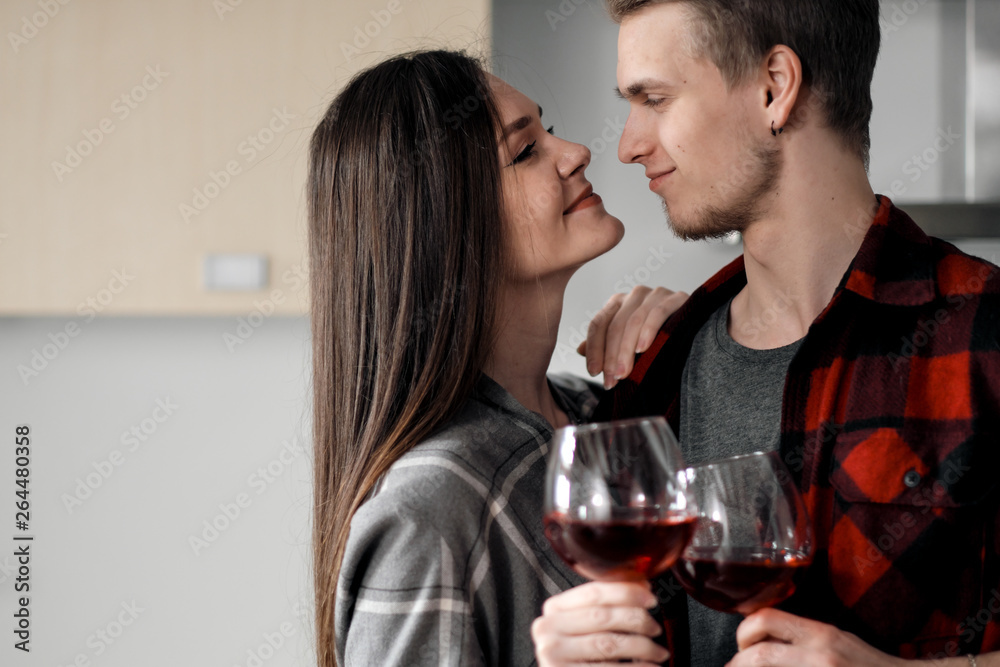 Beautiful young couple in plaid shirts in the kitchen preparing food and drinking red wine from glasses. Beautiful young couple in plaid shirts in the kitchen preparing food and drinking red wine from glasses.
