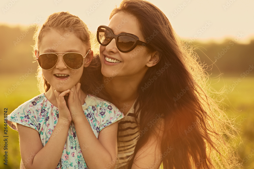 Happy fashion kid girl embracing her mother in trendy sunglasses smiling and looking on nature background. Closeup Happy fashion kid girl embracing her mother in trendy sunglasses smiling and looking on nature background. Closeup