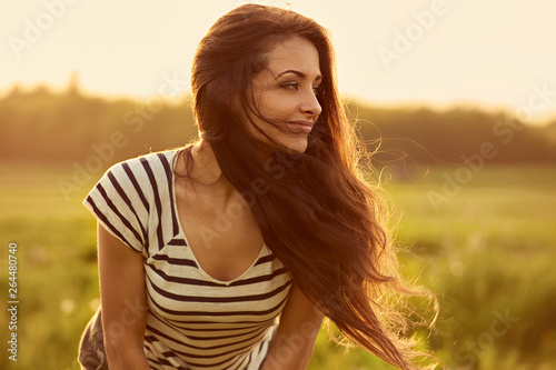 Beautiful smiling young woman looking happy with long amazing bright long hair on nature bright sunset summer background. Closeup © nastia1983