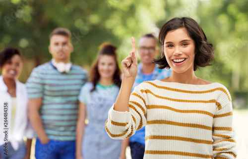 gesture, counting and people concept - happy smiling young woman in striped pullover showing one finger or pointing up over grey background