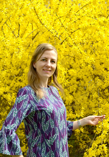 The young woman stands near the blossoming forzition photo