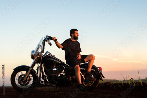 Young man sitting on his custom classic motorcycle admiring the landscape