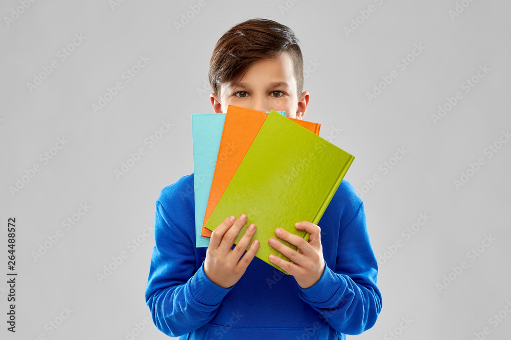 school, education and people concept - shy student boy hiding behind books over grey background school, education and people concept - shy student boy hiding behind books over grey background
