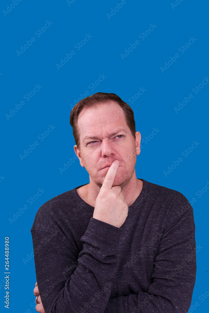 Man in deep thought finger on his lips looking up day dreaming on blue background Man in deep thought finger on his lips looking up day dreaming on blue background