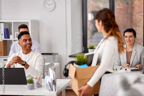 business, new job and quit concept - happy smiling colleagues looking at businesswoman or female employee holding her personal stuff at office