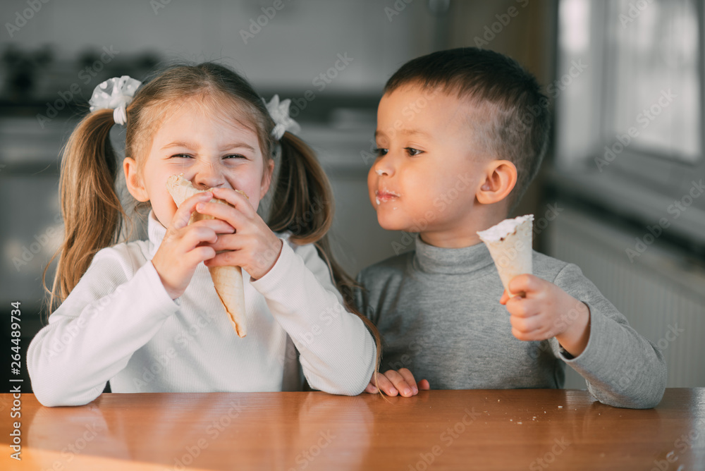 kids boy and girl eating ice cream cone in the kitchen is a lot of fun - obrazy, fototapety, plakaty 