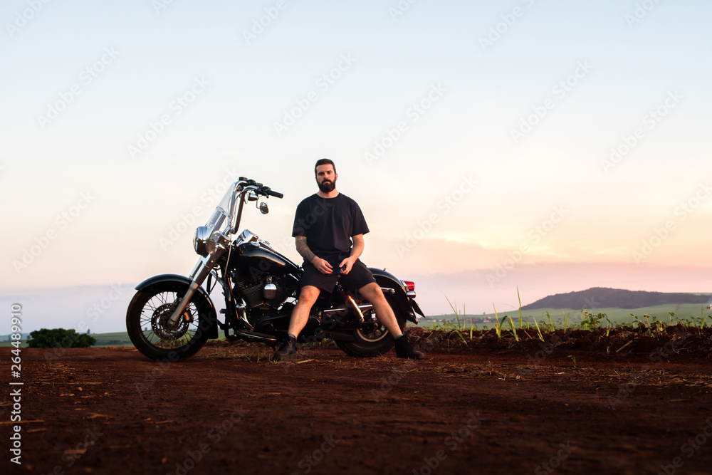 Obraz premium Young man sitting on his custom classic motorcycle admiring the landscape