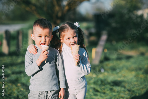 Kids Boy and girl eating ice cream outdoors on grass and trees background