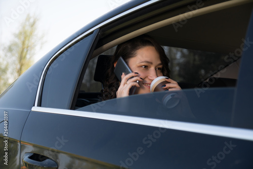 Beautiful female executive talking on her mobile phone and drink coffee in the car © Daniel