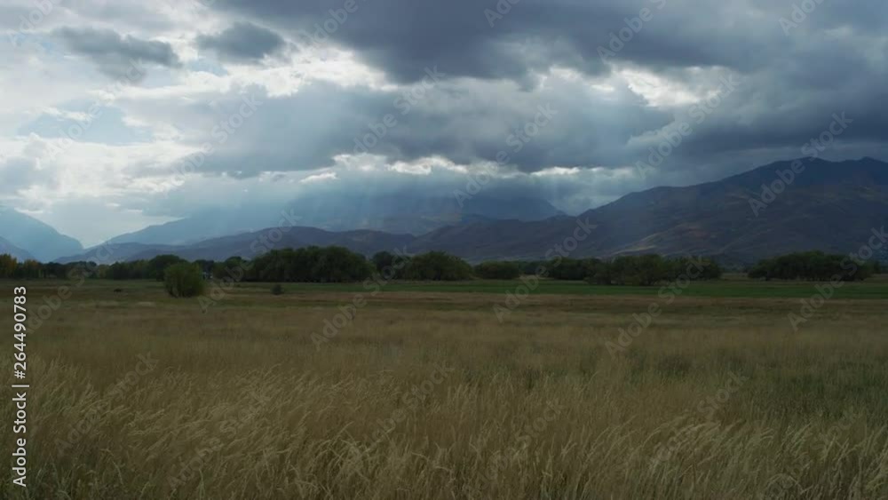 Tilt up to sunbeams shining through clouds over windy field near mountain range / Heber City, Utah, United States Tilt up to sunbeams shining through clouds over windy field near mountain range / Heber City, Utah, United States