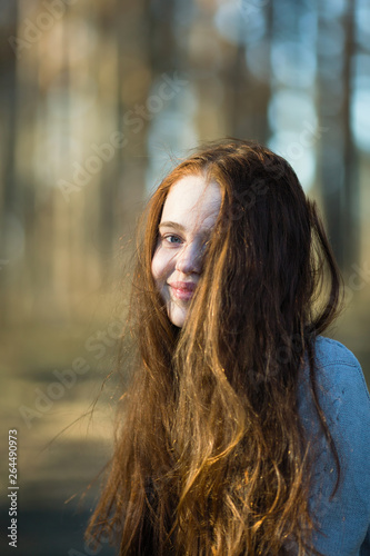Portrait of pretty young girl with long bright red hair outdoors.