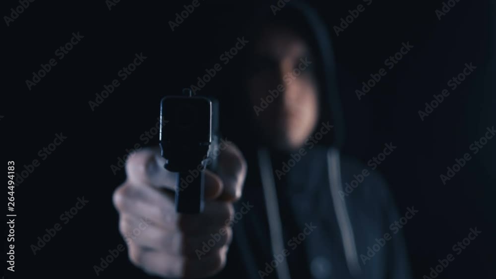 Dangerous hooded Criminal aims his Gun on black background. Focus is on the barrel with a one hand pistol grip. Dangerous hooded Criminal aims his Gun on black background. Focus is on the barrel with a one hand pistol grip.