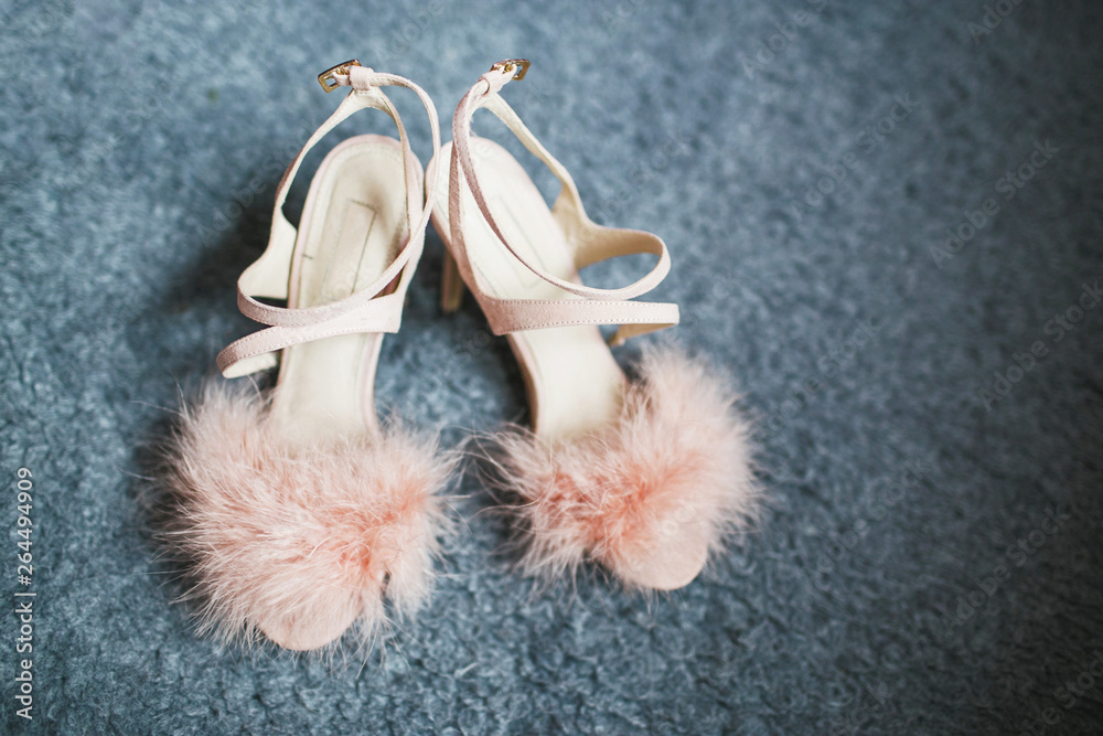 Fluffy pink wedding shoes on gray carpet.