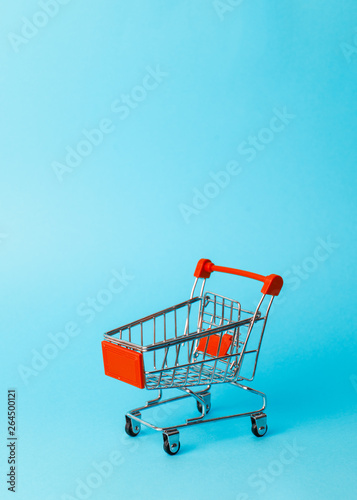 Women's shopping: an empty miniature red trolley from a supermarket on a blue background.