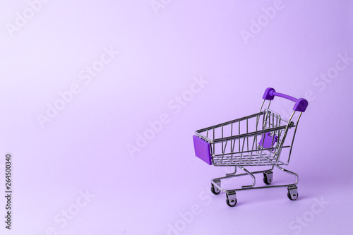 Women's shopping: an empty miniature purple trolley from a supermarket on a purple background.