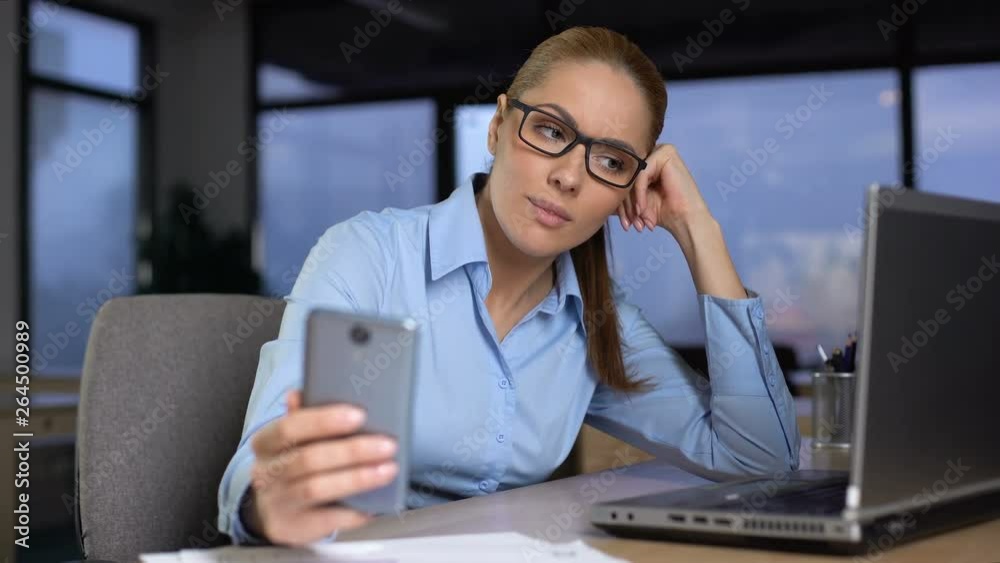 Woman typing message on mobile phone instead of working, bored at unloved job Woman typing message on mobile phone instead of working, bored at unloved job
